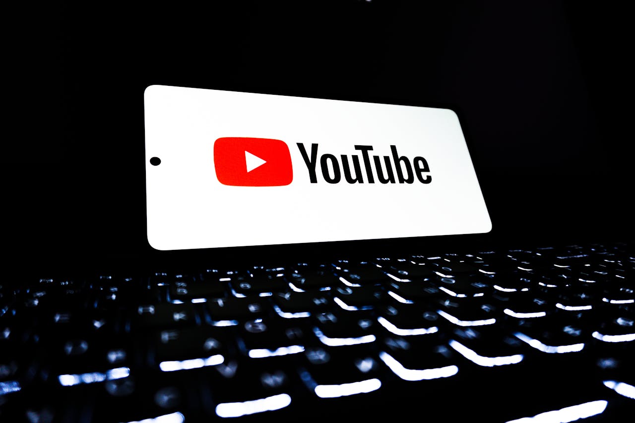 YouTube app icon displayed on a smartphone over an illuminated keyboard, representing digital media and online streaming.